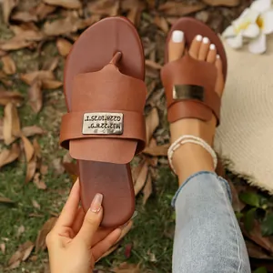 Nahaufnahme von braunen flachen Zehentrenner-Sandalen mit dekorativer Metallplatte