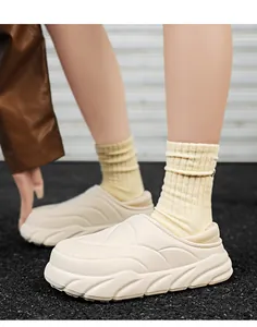Nahaufnahme von cremefarbenen wattierten Winterslippern mit Steppmuster und dicker Sohle.