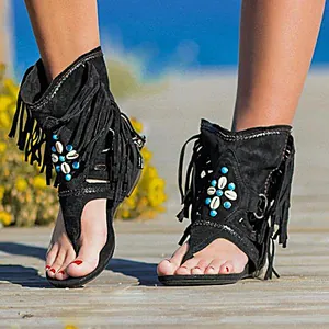 Detalle de sandalias boho negras con flecos, cuentas turquesas y adornos de conchas