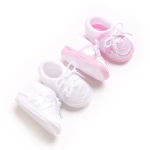 Détail de la broderie cœur et du nœud sur ces chaussons de sol bébé rose et blanc.
