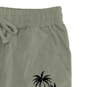 Detail of men's olive green linen pants featuring a palm tree print and drawstring waist