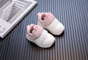 Close-up of pink and white baby walking shoes with 'Fashion' velcro on black surface