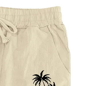 Close-up detail of men's beige cotton linen pants with drawstring and palm tree print.