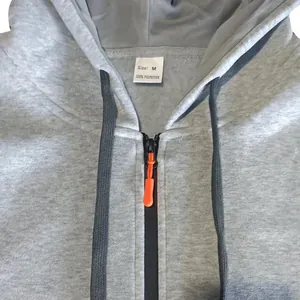 Detailed view of a grey men's zip-up hoodie with black drawstrings and orange zipper pull.