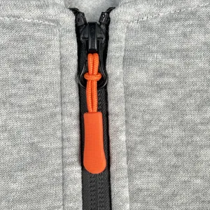 Close-up of the textured orange zipper puller on a grey fleece hoodie