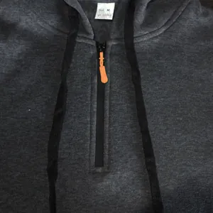 Close-up detail of grey hoodie featuring half-zip with orange pull and drawstrings