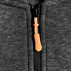 Macro view of bright orange rubberized zipper pull on textured grey fleece hoodie fabric