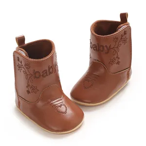 Detailed macro view of brown PU leather baby boots with embroidered baby text and flowers
