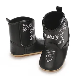 Detailed close-up shot of black baby boots with white floral and baby text embroidery