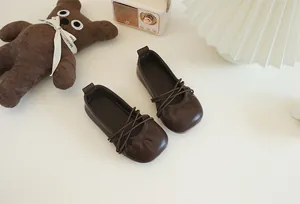 Nahaufnahme von dunkelbraunen Leder-Ballerinas für Mädchen mit elastischen Überkreuzriemen.
