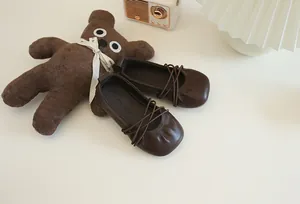 Nahaufnahme von braunen Leder-Ballerinas für Mädchen mit gekreuzten Riemen und weicher Sohle.