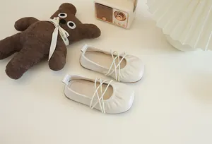 Detailansicht cremefarbener Kinder-Ballerinas mit einem eleganten Kreuzgurt-Design.