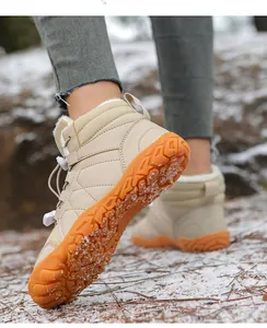 Close-up of beige winter snow boots with orange anti-slip soles in a snowy outdoor setting.