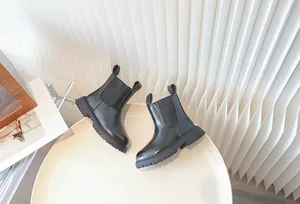 Classic black children's Chelsea boots with chunky lug soles on a stylish white tray