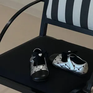 Detail of silver quilted girls' shoes with black bow on a striped chair.