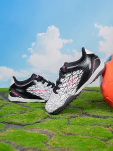 Detail view of durable synthetic children's soccer shoes on turf with a football.