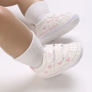 Close-up of white toddler sneakers featuring embroidered pink hearts and velcro straps
