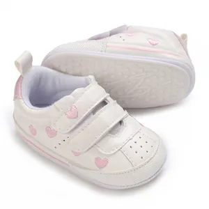 Detailed close-up view of white baby sneakers featuring pink heart embroidery and non-slip sole