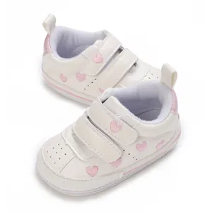 Detailed macro shot of white baby sneakers featuring pink heart embroidery and Velcro straps
