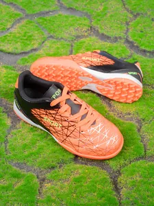 Close-up of orange kids' soccer shoes with turf cleats on artificial grass.