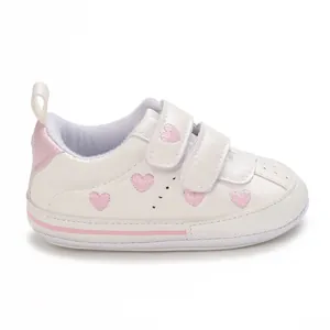 Detailed side view of white baby sneaker featuring pink heart embroidery and velcro straps.