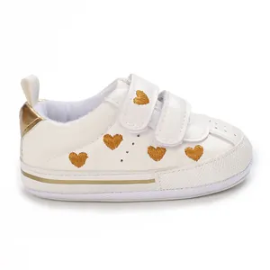 Detail of white baby sneakers featuring gold heart embroidery and velcro straps.