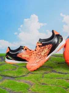 Professional orange and black turf soccer shoes for kids boys age 6-12 on grass field