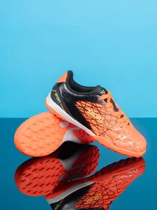 Detail view of orange and black kids soccer shoes with turf studs and mesh pattern
