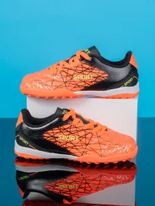 Side view of orange and black kids' turf soccer shoes with spiderweb pattern and cleats.