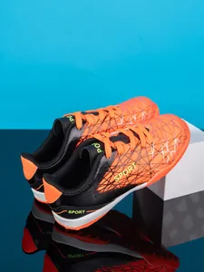 Detail view of orange and black kids' soccer shoes with geometric patterns and SPORT logo