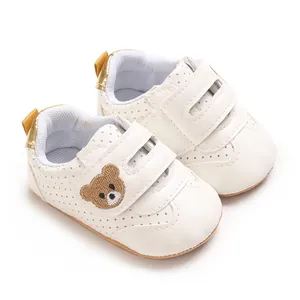 Primer plano de zapatos blancos para bebé con bordado de osito y detalles perforados.