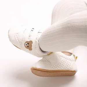Primer plano de zapatos blancos para bebé con un lindo parche de oso bordado