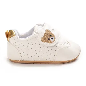 Detalle de zapato blanco para bebé con bordado de oso y cierre de correa ajustable