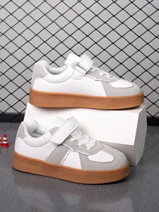Detalle de zapatillas infantiles blanco y gris con suela de goma marrón y cierre de velcro.