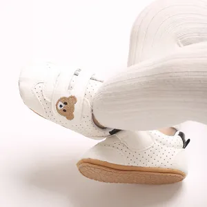 Detalle de zapatos blancos para primeros pasos con bordado de oso y suelas de goma suaves