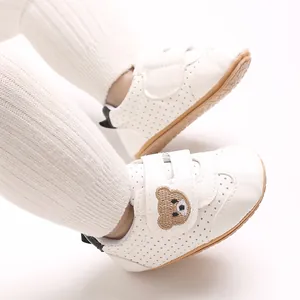 Primer plano de zapatos para caminar para bebé blancos con bordado de oso pardo en la correa