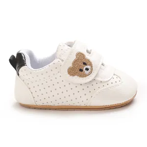 Primer plano de zapatos blancos para bebés con un bordado de oso en la tira de velcro