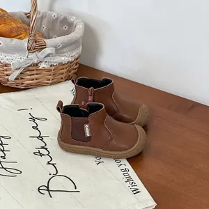 Close-up of brown children's leather Chelsea boots on a rustic wooden table setting.