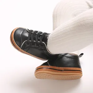 Detailopname van zwarte babywandelschoenen met zachte rubberen zolen en witte leggings.