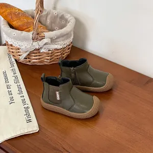 Detailed view of olive green toddler boots with soft rubber soles on a wooden table
