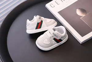 Macro detail of white infant walking shoes featuring red and green side stripes and velcro.