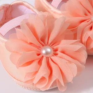 Détail macro de chaussures bébé pêche avec fleurs en mousseline et perle centrale.