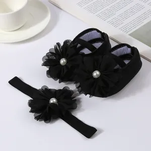 Vue détaillée de chaussures pour bébé noires et d'un bandeau assorti avec fleurs en mousseline.