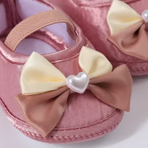 Close-up detail of pink baby girl dress shoes with elegant double bow and heart pearl accent
