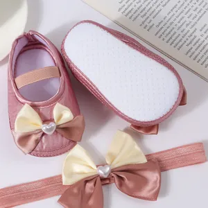 Close-up detail of pink satin baby princess shoes and matching bow headband set for newborns
