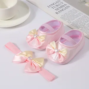Close-up of pink satin baby princess shoes with bow and pearl heart detail.