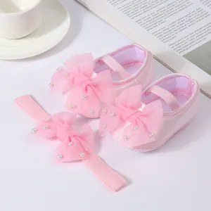 Close-up of pink satin baby shoes and matching headband set with elegant pearl bows.