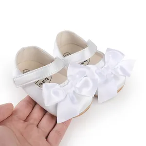 Macro detail of elegant white satin baby shoes featuring large bows, held for scale