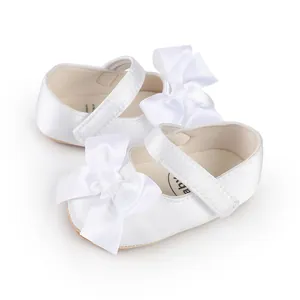 Close-up view of elegant white satin baby walking shoes with large bow decoration