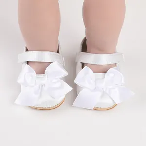 A close-up detailed view of white satin baby walking shoes with a large decorative bow